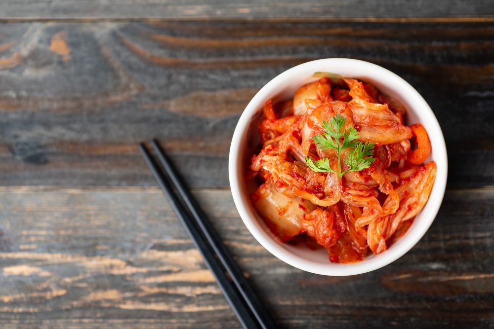 Kimchi cabbage in a bowl with chopsticks for eating on wooden background, top view, Korean food
